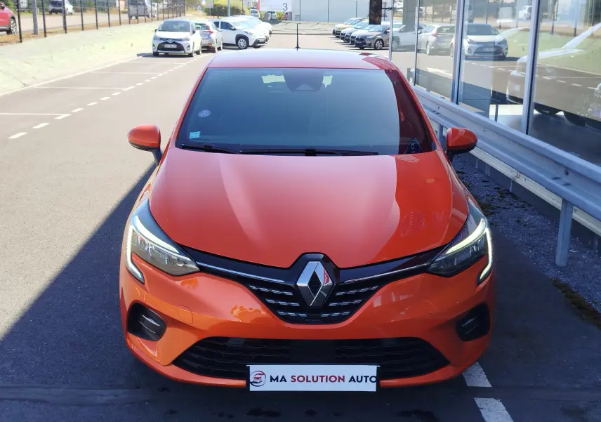 Vue avant d'une Renault Clio 1.6 E-Tech hybride 140ch Intens 2022 en orange Valencia avec phares LED allumés.