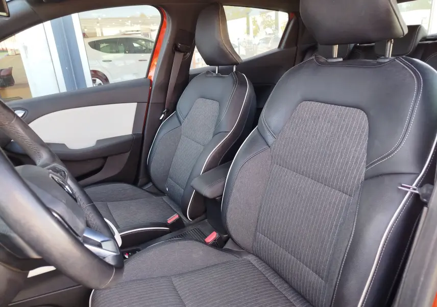 Vue intérieure côté conducteur de la Renault Clio orange Valencia 2022, sièges tissu gris et cuir noir avec surpiqûres blanches.