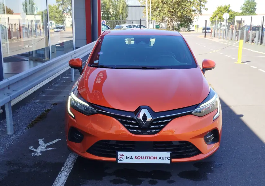 Vue avant d'une Renault Clio 1.6 E-Tech hybride 140ch Intens 2022 en Orange Valencia avec phares LED allumés.