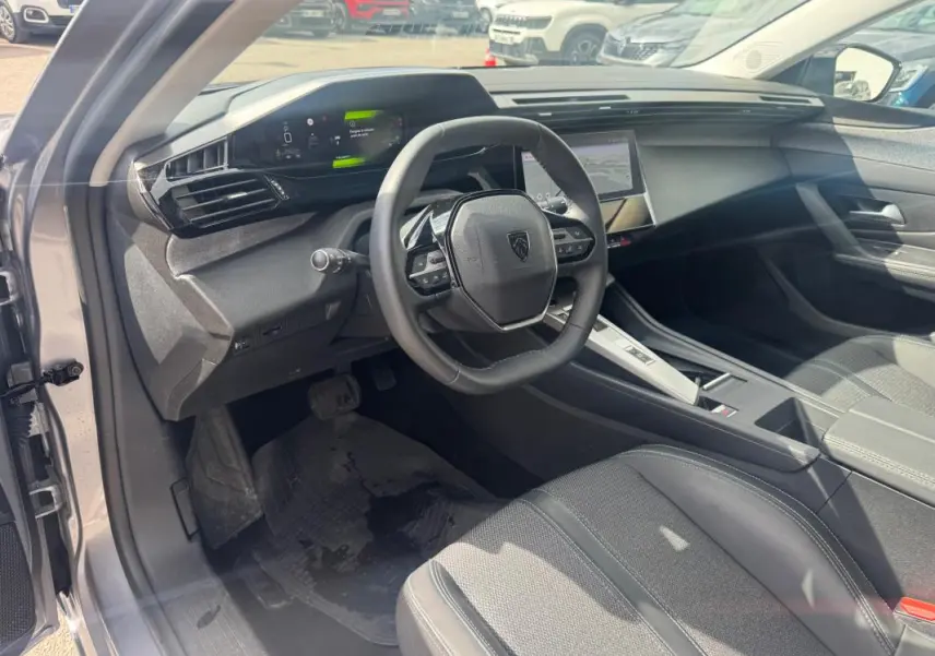 Vue intérieure côté conducteur de la Peugeot 308 Hybrid gris 2025, avec volant compact et cockpit numérique lumineux.