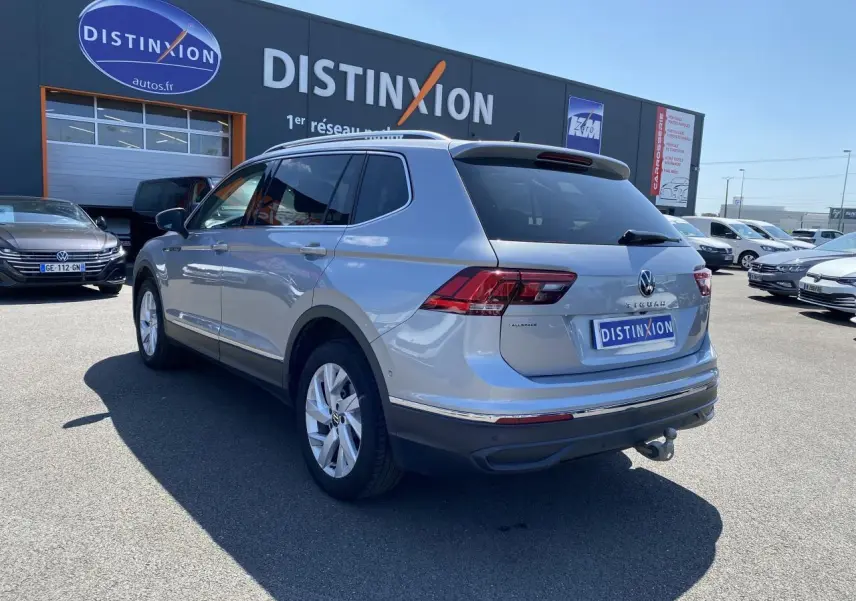 Volkswagen Tiguan Allspace gris argent vu en 3/4 arrière droit avec crochet d'attelage escamotable et vitres teintées.