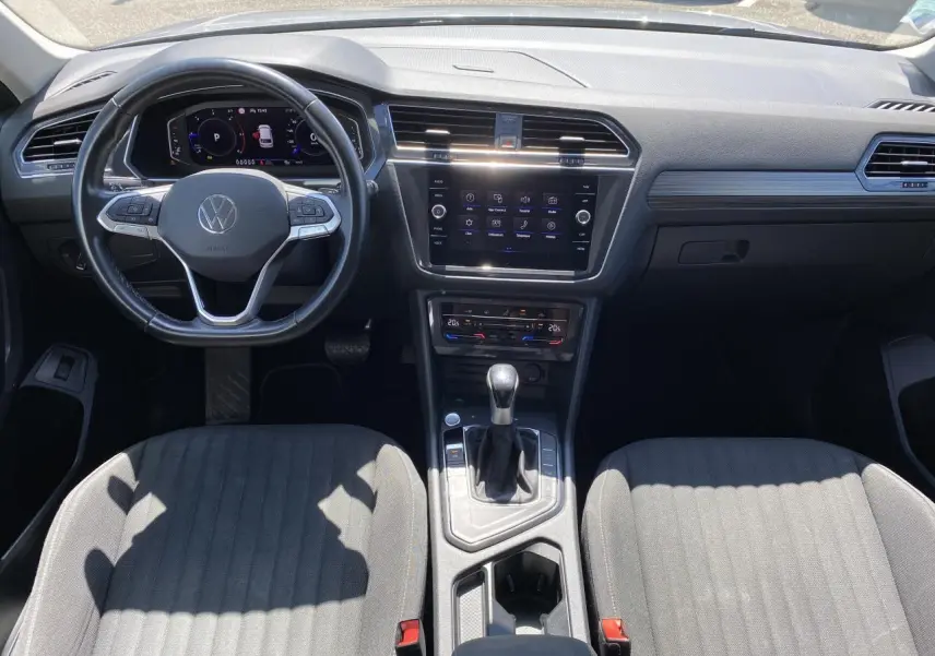 Vue intérieure avant du Volkswagen Tiguan Allspace 2022, tableau de bord moderne avec écran tactile et sellerie tissu gris.