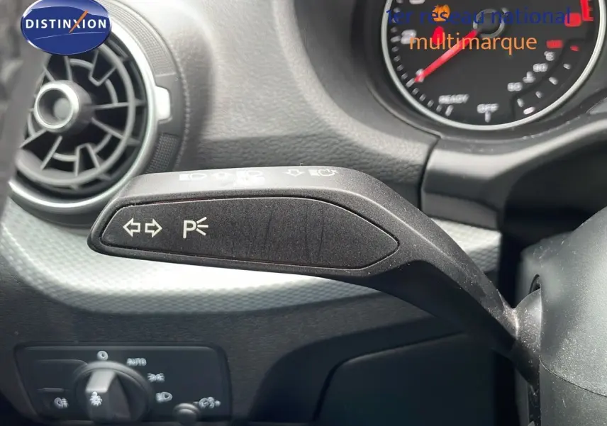 Gros plan sur la commande de clignotants à gauche du volant d'un Audi Q2 noir mito metal, tableau de bord en arrière-plan.