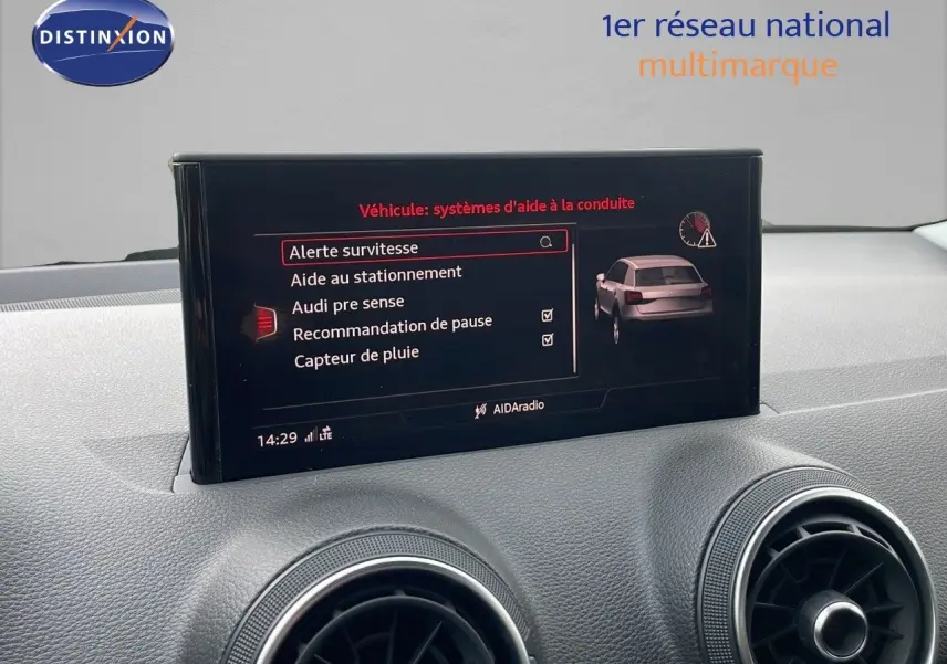 Écran central de l'Audi Q2 35 TFSI 2023 affichant les aides à la conduite, intérieur gris et aérateurs ronds visibles.
