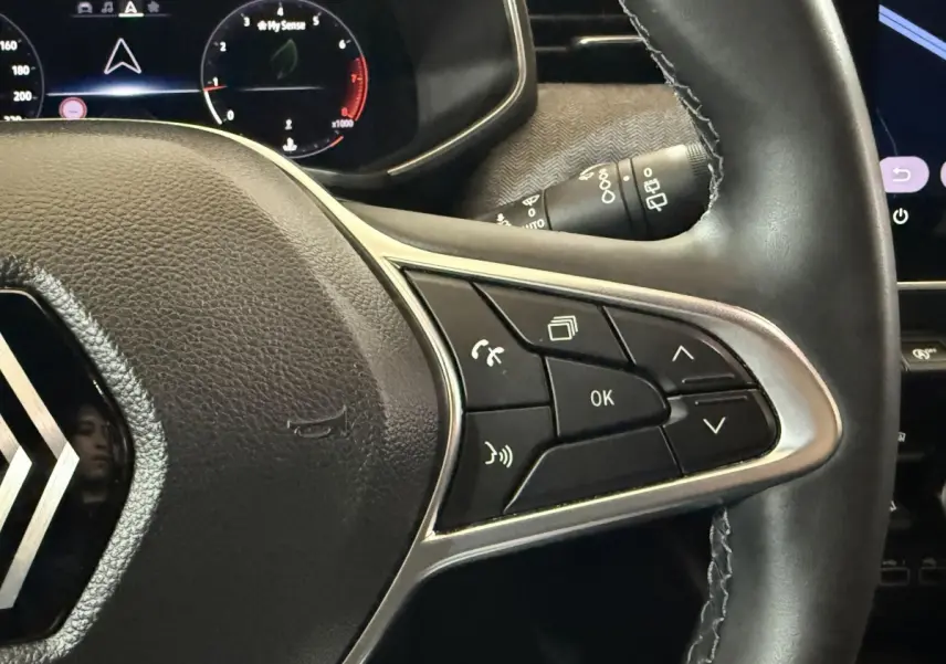 Gros plan sur le volant cuir noir de la Renault Clio 2024 avec commandes multifonctions côté droit et combiné numérique en arrière-plan.
