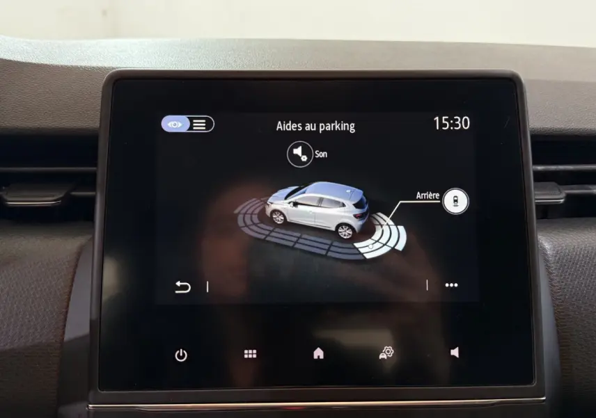Écran tactile intérieur montrant l'aide au parking arrière d'une Renault Clio blanche, vue de dessus stylisée.