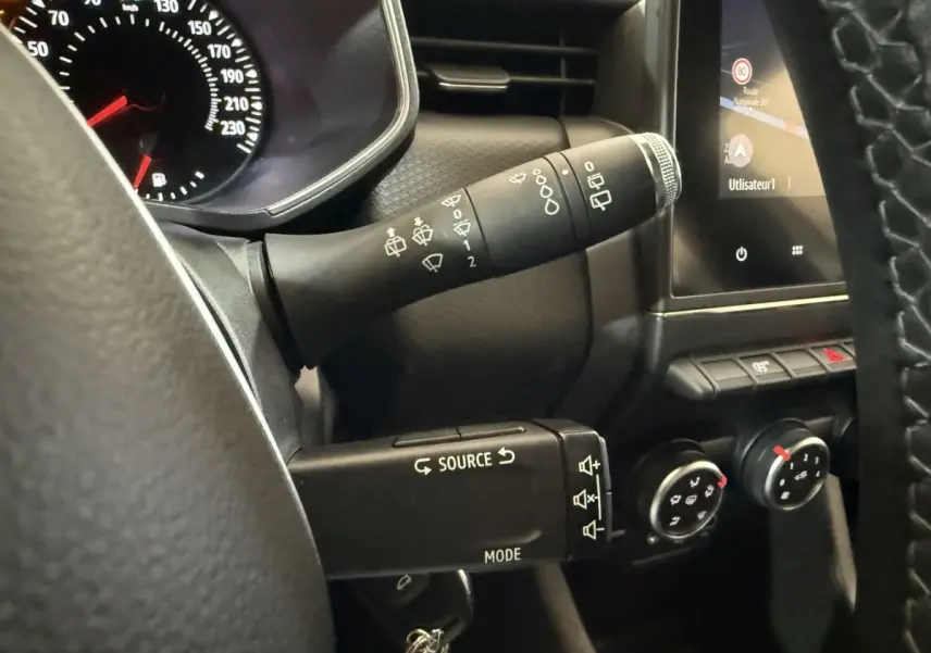 Gros plan sur le volant et la commande des essuie-glaces d’une Renault Clio Business blanche, avec écran tactile et commandes de climatisation.