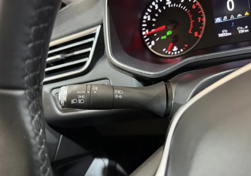 Gros plan sur la manette des feux et clignotants à gauche du volant cuir synthétique dans le tableau de bord de la Renault Clio blanche.