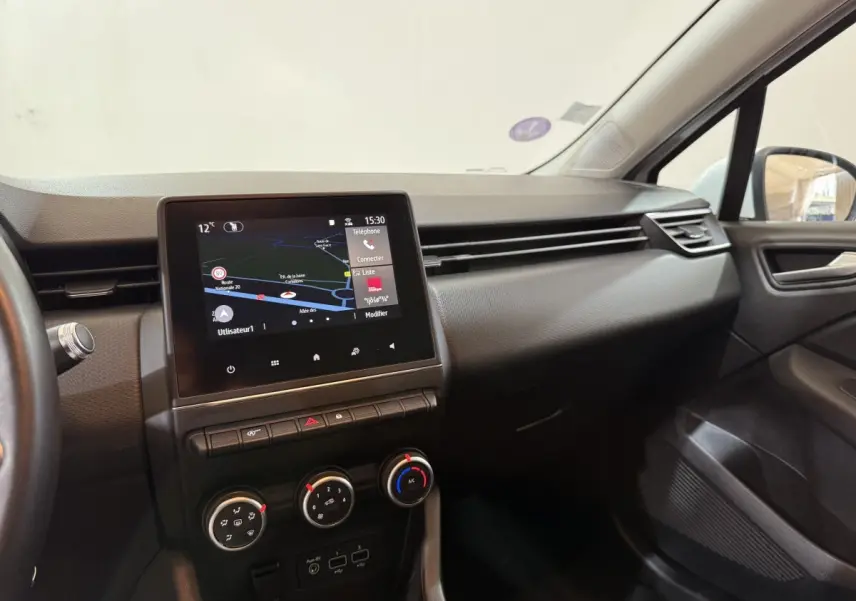 Vue intérieure côté passager de la Renault Clio Business blanche, avec écran tactile de navigation et commandes de climatisation.