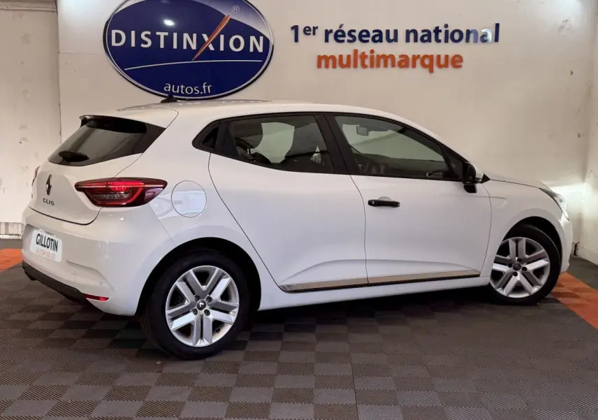 Profil droit d'une Renault Clio Business blanche de 2021, avec jantes alliage et feux arrière LED visibles en intérieur showroom.