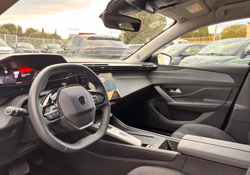 Intérieur de la Peugeot 308 Hybrid 145 gris, vue côté conducteur montrant le volant compact et le cockpit numérique.