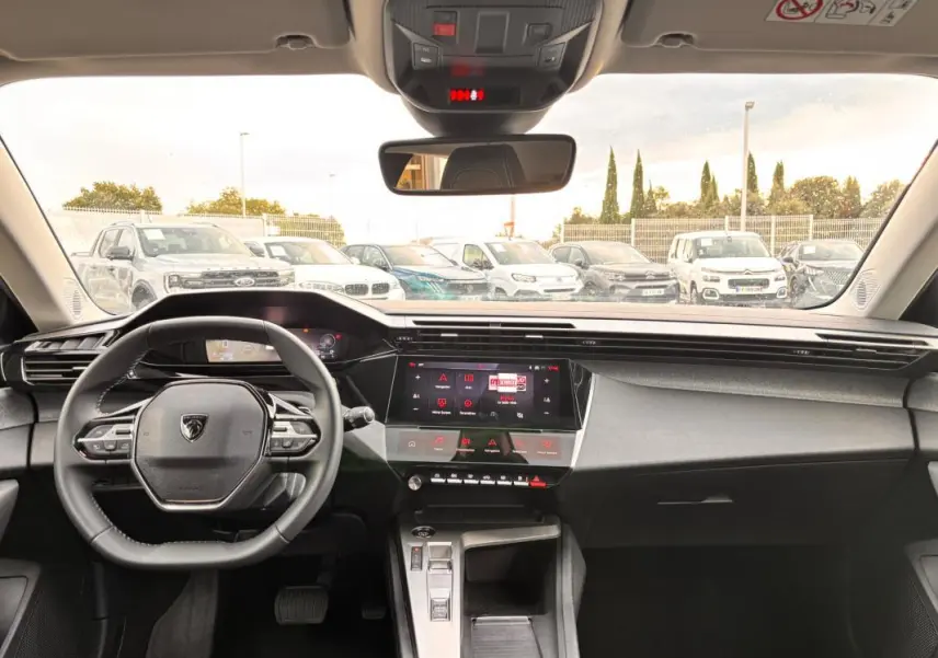 Vue intérieure frontale du cockpit numérique gris de la Peugeot 308 Hybrid 145 e-DCS6 Allure avec volant compact et écran tactile central.