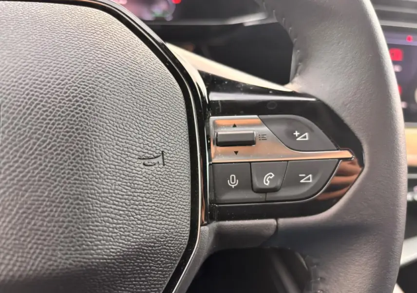 Gros plan sur le volant noir du Peugeot 308 Hybrid 145 e-DCS6 Allure avec commandes audio et téléphone intégrées.
