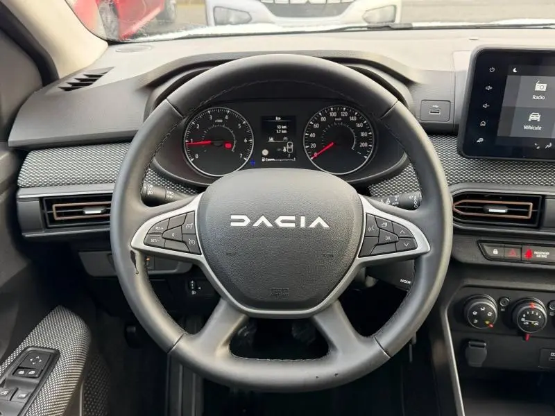 Vue intérieure centrée sur le volant du Dacia Sandero 2025, tableau de bord moderne avec écran tactile et commandes au volant.