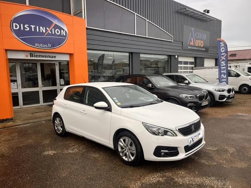 PEUGEOT 308 blanc banquise vue 3/4 avant droit, garée devant un concessionnaire avec plusieurs autres véhicules.