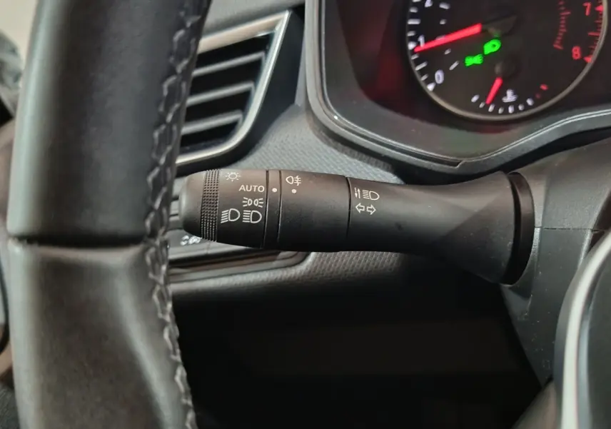 Gros plan sur la manette des phares et clignotants à gauche du volant cuir synthétique d’une Renault Clio gris clair 2023.