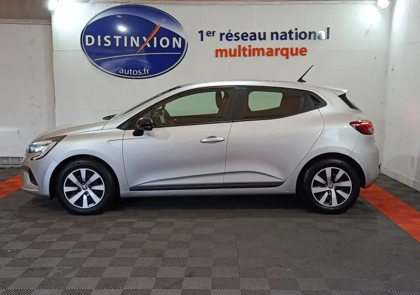 Profil droit d'une Renault Clio 2023 gris clair, avec jantes alliage et feux arrière LED visibles en intérieur showroom.