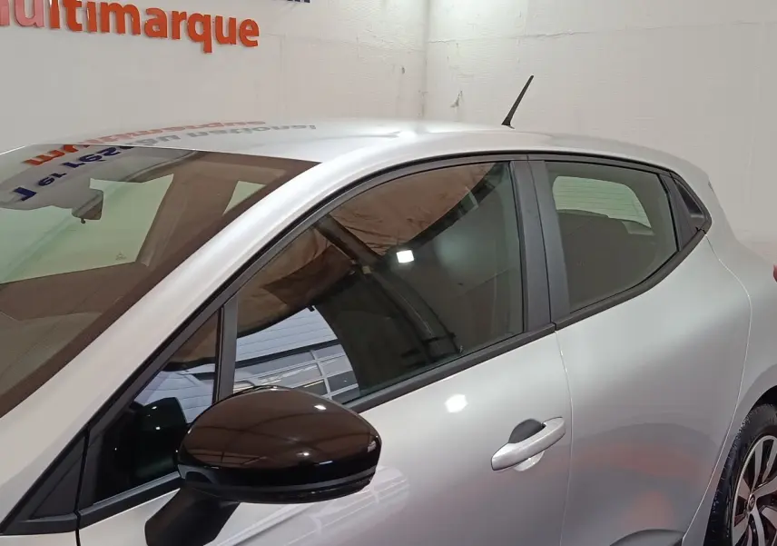 Profil droit de la Renault Clio Equilibre TCe 90 gris clair avec rétroviseur noir et jantes alliage visibles en intérieur showroom.