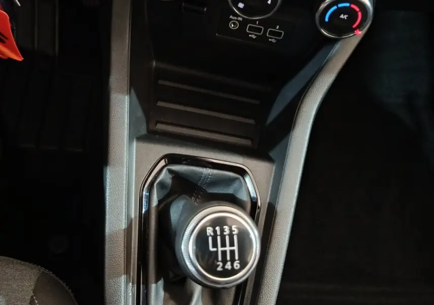 Vue plongeante sur la console centrale de la Renault Clio gris clair 2023, mettant en valeur le levier de vitesses manuel et les commandes de climatisation.