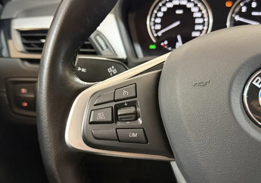 Gros plan sur le volant cuir et alu de la BMW X2 sDrive18i 2023, avec commandes multifonctions côté gauche.