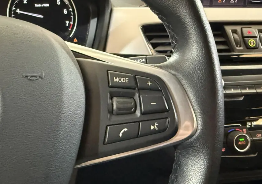 Gros plan sur le volant cuir noir de la BMW X2 sDrive18i Lounge 2023 avec commandes multifonctions visibles.