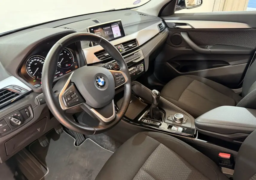 Vue intérieure côté conducteur de la BMW X2 sDrive18i Lounge 2023, tableau de bord et volant cuir multifonctions.