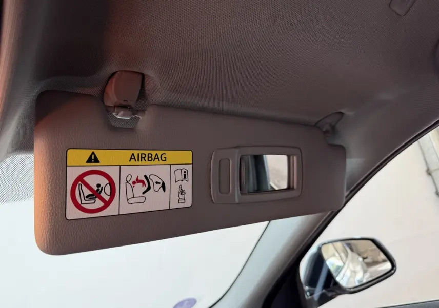 Détail du pare-soleil gris avec miroir intégré et avertissement airbag, côté gauche intérieur d'une BMW X2 blanc.