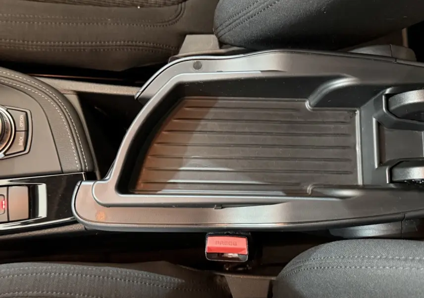 Vue rapprochée de la console centrale noire avec molette de sélection et accoudoir entre les sièges avant gris foncé du BMW X2 sDrive18i Lounge.