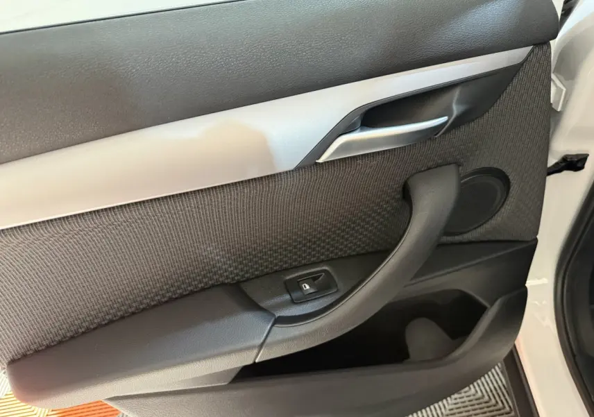 Détail de la porte intérieure côté conducteur d’une BMW X2 sDrive18i blanche, avec poignée noire et insert gris.