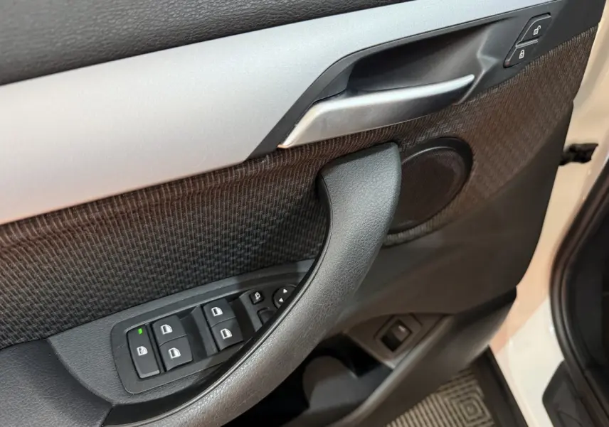 Gros plan sur la porte avant gauche blanche d'une BMW X2 2023, avec commandes de vitres et poignée intérieure noire.