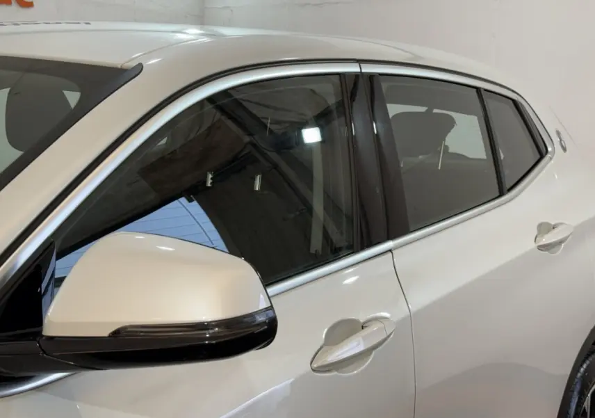 Vue latérale gauche rapprochée du BMW X2 sDrive18i Lounge blanc, mettant en valeur la poignée et le rétroviseur.