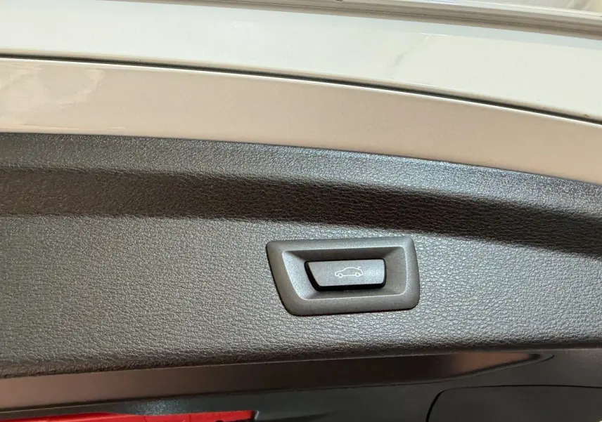 Bouton d'ouverture électrique du coffre sur le hayon intérieur d'un BMW X2 blanc, vue rapprochée.