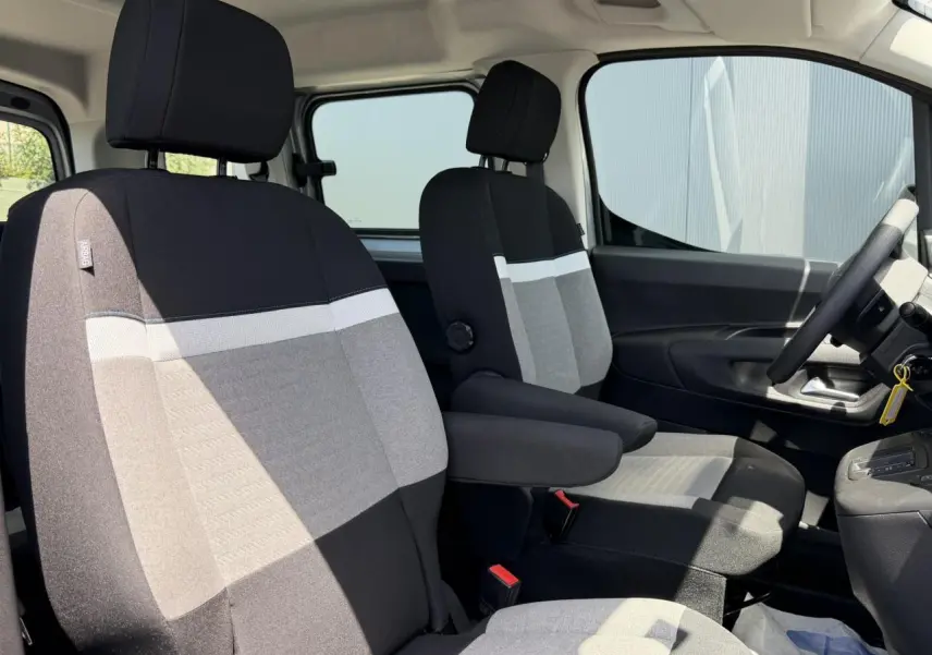 Vue intérieure côté conducteur du Citroën Berlingo ë-136 2025, sièges tissu bicolore gris et noir avec accoudoirs.