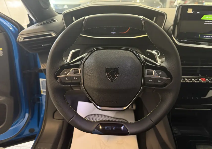 Volant cuir noir avec logo Peugeot et badge GT, vue frontale depuis le siège conducteur du Peugeot 2008 bleu Vertigo 2025.