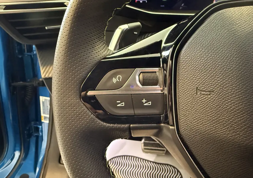 Gros plan sur le volant perforé côté gauche du Peugeot 2008 bleu Vertigo Metal avec commandes audio intégrées.