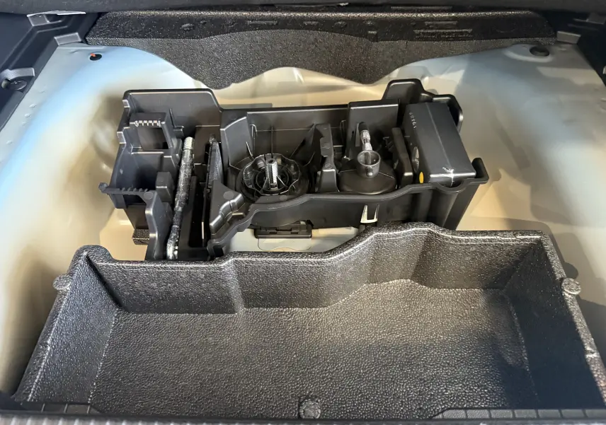 Vue rapprochée du rangement à outils dans le coffre d'un Peugeot 2008 2025 bleu Vertigo avec toit noir.