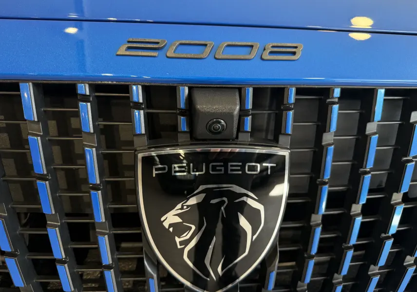 Gros plan sur la calandre bleu vertigo métallisé du Peugeot 2008 avec logo lion et caméra frontale intégrée.