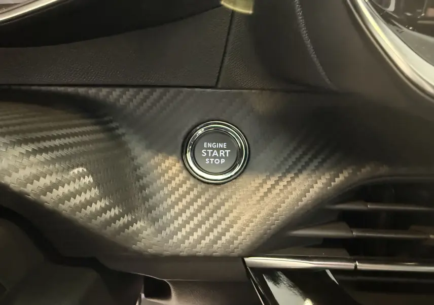 Gros plan sur le bouton start/stop entouré d'un habillage noir effet carbone dans l'habitacle du Peugeot 2008.