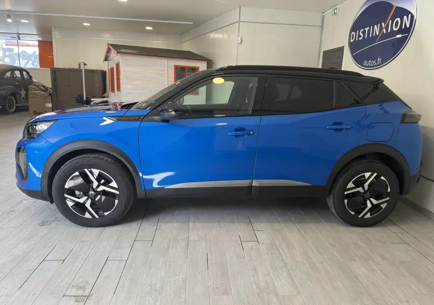 Profil droit d'un Peugeot 2008 GT 2025 bleu Vertigo avec toit noir, roues stylées et détails noirs contrastants.