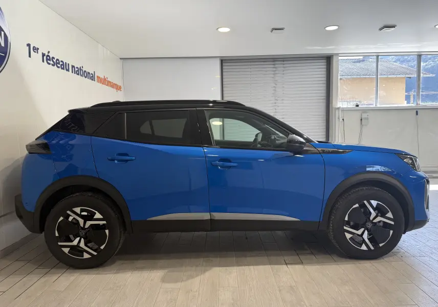 Peugeot 2008 GT bleu Vertigo métal avec toit noir, vue de profil côté gauche en intérieur showroom.