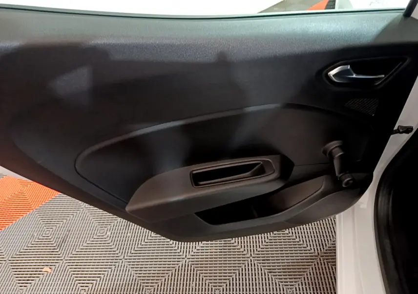 Vue intérieure du panneau de porte côté gauche d'une Renault Clio blanche, avec poignée et commande de vitre manuelle.