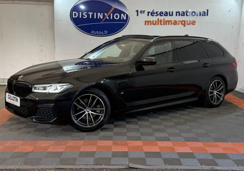 BMW Série 5 Touring 520d noir vue de profil droit en intérieur avec jantes M Sport et phares LED allumés.