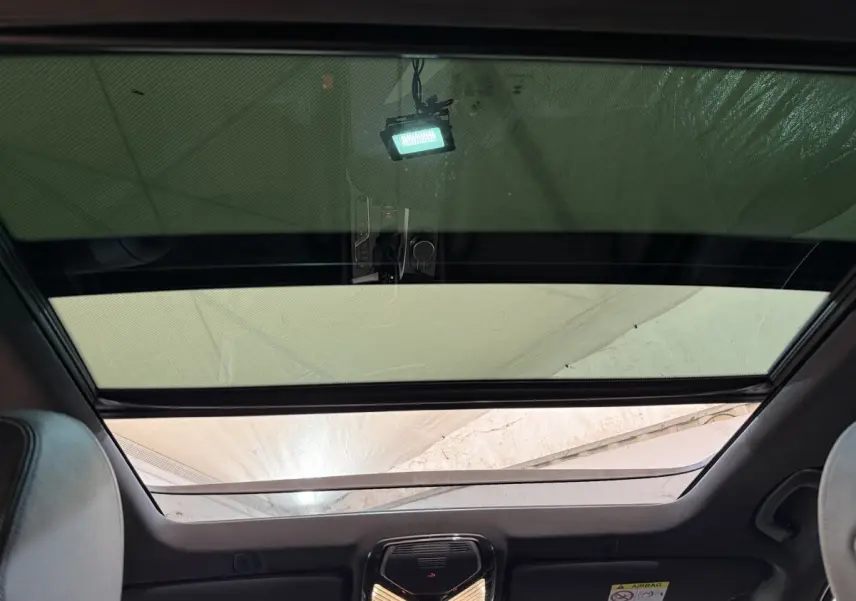 Vue intérieure du toit ouvrant panoramique avec pare-soleil partiellement fermé sur BMW Série 5 Touring noir.