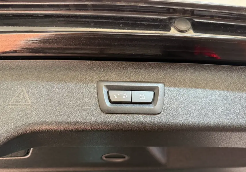 Gros plan sur les boutons de fermeture et verrouillage du coffre de la BMW Série 5 Touring noire, version 520d M Sport.