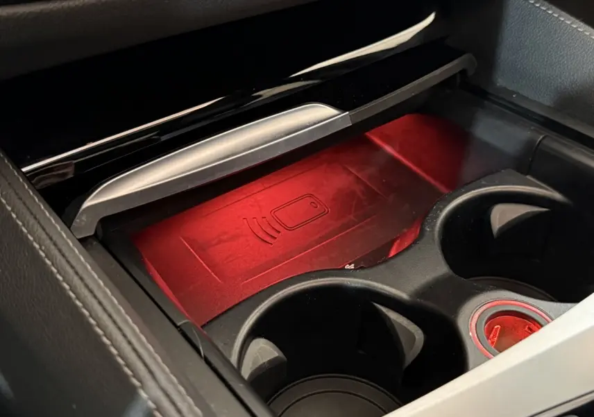 Gros plan sur le compartiment central noir avec éclairage rouge et zone de recharge sans fil dans BMW Série 5 Touring 520d 2023.