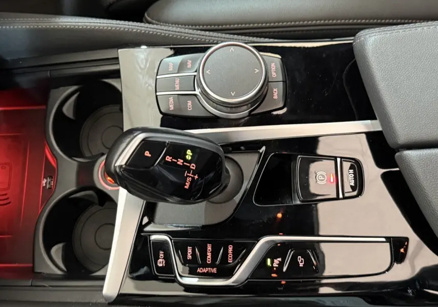 Vue rapprochée de la console centrale noire brillante de la BMW Série 5 Touring 520d avec levier de vitesses automatique et commandes.