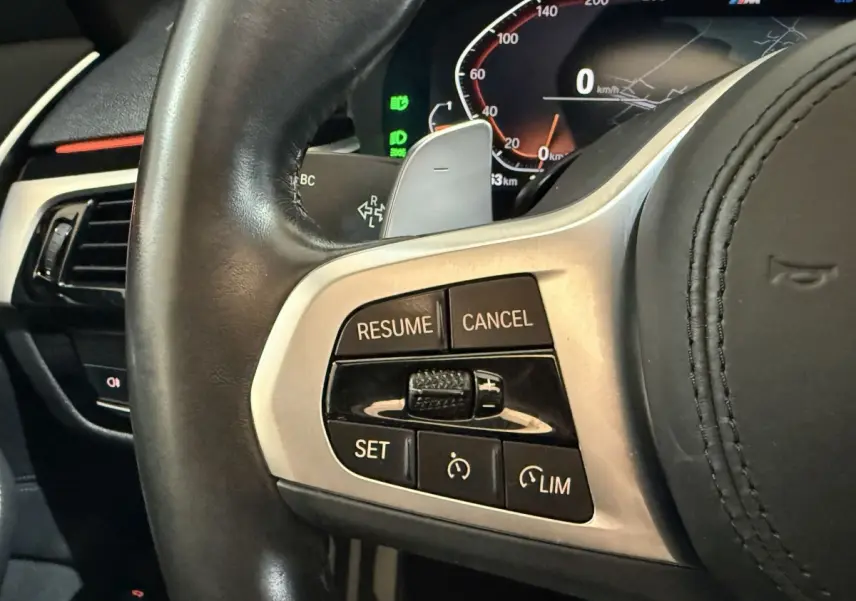 Gros plan sur le volant cuir noir de la BMW Série 5 Touring 520d M Sport 2023, avec commandes de régulateur de vitesse.