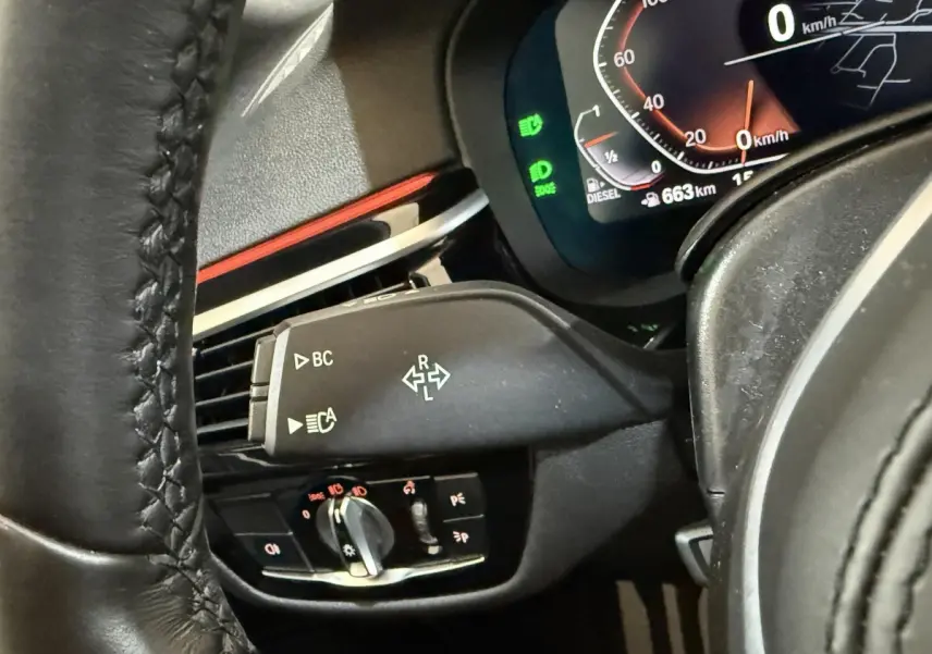 Gros plan sur la commande de clignotants et tableau de bord numérique d'une BMW Série 5 Touring noire, côté gauche du volant.