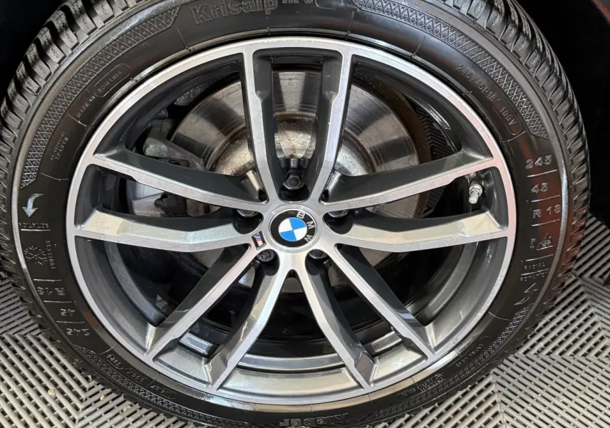 Gros plan sur la jante alliage bicolore et le pneu hiver d'une BMW Série 5 Touring noire.