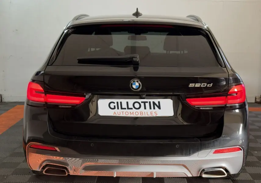 Vue arrière d'une BMW Série 5 Touring 520d noire avec feux LED allumés et double sortie d'échappement chromée.